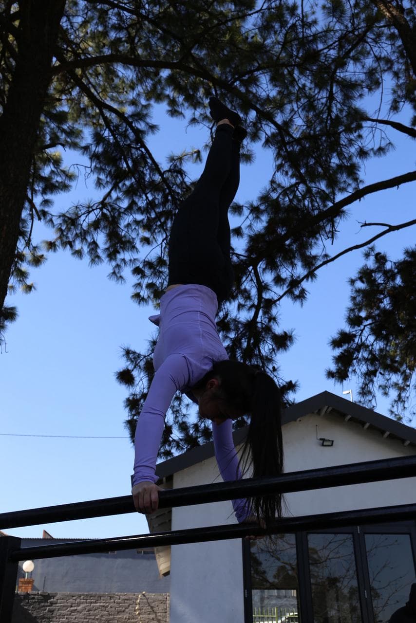 Athlete holding a handstand on a high bar, silhouetted against the evening sky
