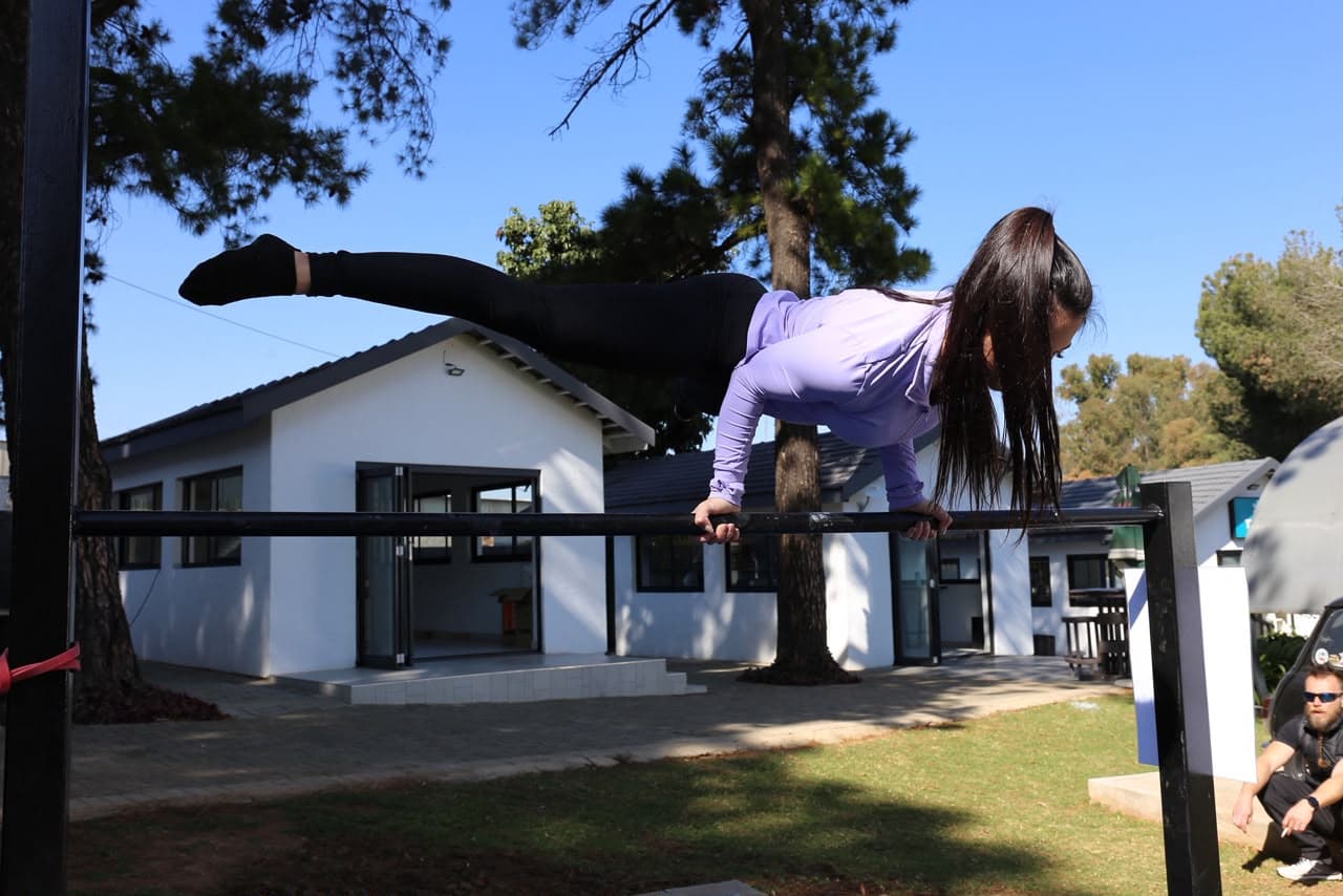 Athlete holding a front lever on a high bar under clear sky at the Elevate Athletic park