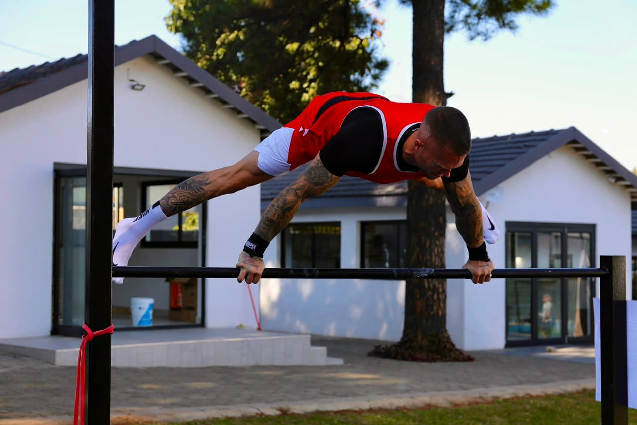 Athlete holding a straddle planche on a low bar at the park